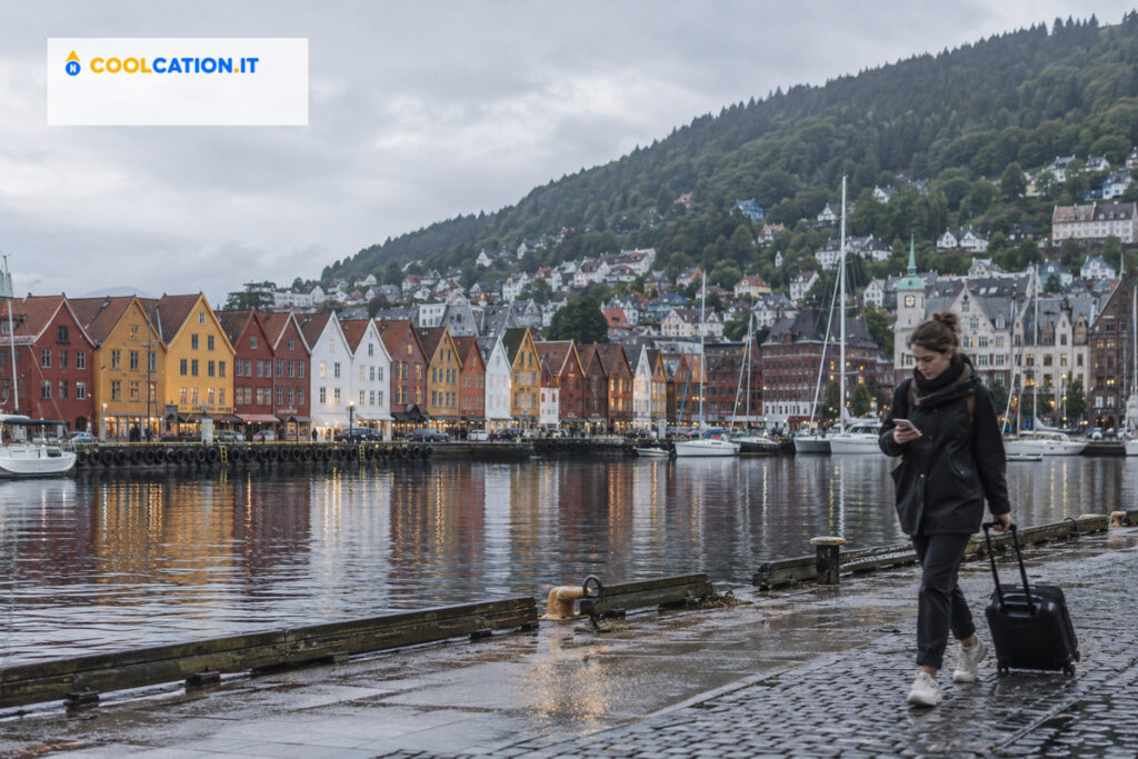 Porto di Bergen con le case in legno di Bryggen e una viaggiatrice con valigia sul lato destro